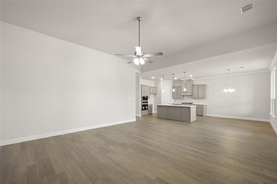 Unfurnished living room with baseboards, wood finished floors, a chandelier, recessed lighting, and crown molding Unfurnished living room with baseboards, wood finished floors, a chandelier, recessed lighting, and crown molding