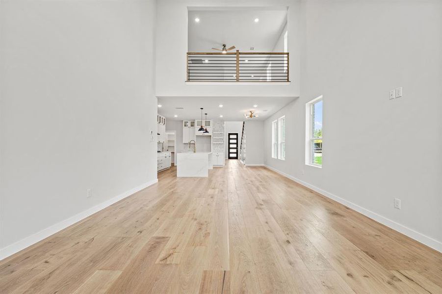 Unfurnished living room with a towering ceiling, sink, and light wood-type flooring