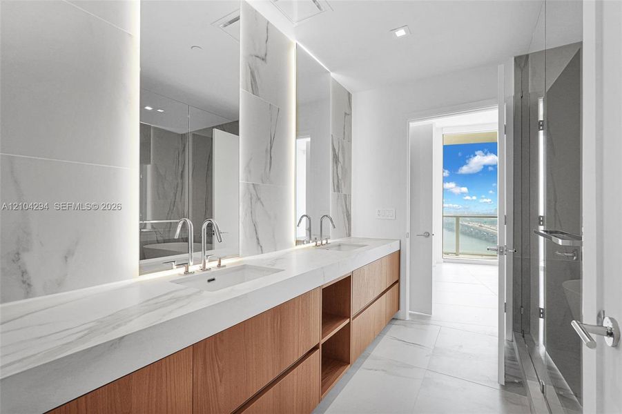 Dual vanity with integrated sinks, wood-finish cabinetry, polished chrome fixtures, and large format wall and floor tiling