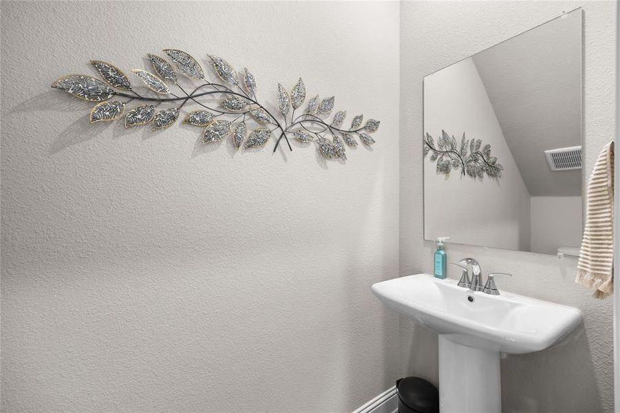 This convenient powder bath was a chosen owner upgrade, featuring a stylish pedestal sink and a framed mirror. This thoughtfully placed half-bath is perfect for guests and adds excellent functionality to the home's layout.