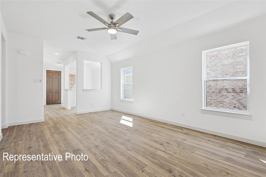 Spacious room featuring wood-finish flooring, crisp white walls, and a contemporary ceiling fan with integrated lighting