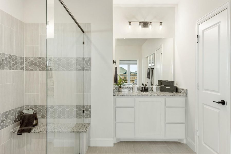 Bathroom with glass walk-in shower, white vanity, granite countertop, and hexagon tile accents