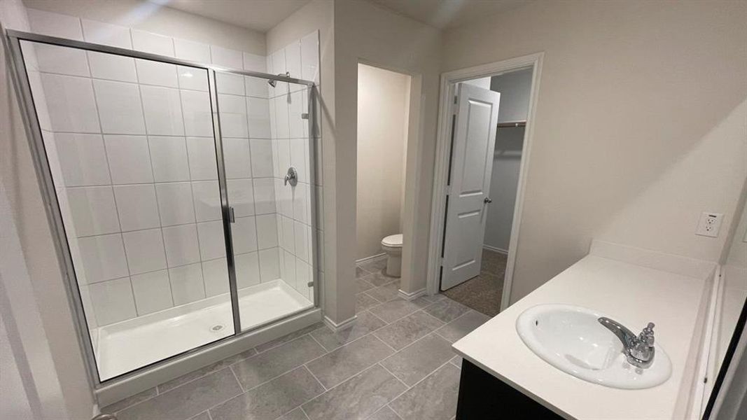 Bathroom featuring a spacious walk-in shower with tile surround and glass enclosure, a single vanity with an integrated sink and chrome faucet, and large format floor tiling