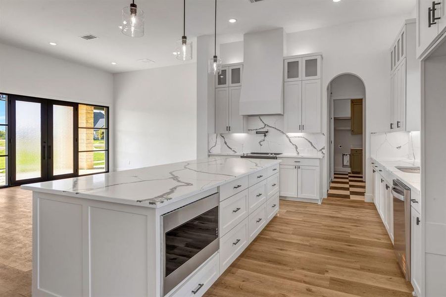 Kitchen with light stone counters, glass insert cabinets, pendant lighting, appliances with stainless steel finishes, and white cabinetry