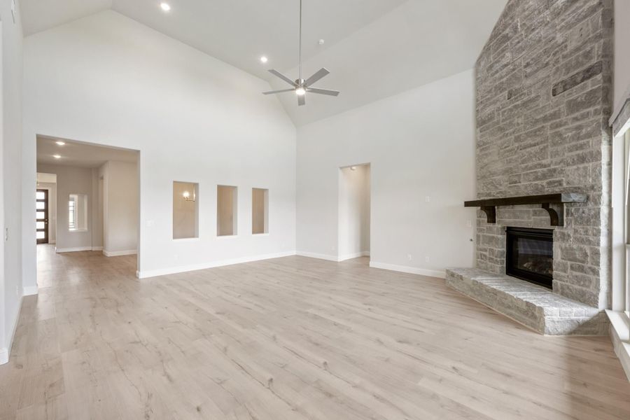 Open living room with vaulted ceiling, stone fireplace, ceiling fan, and light hardwood floors