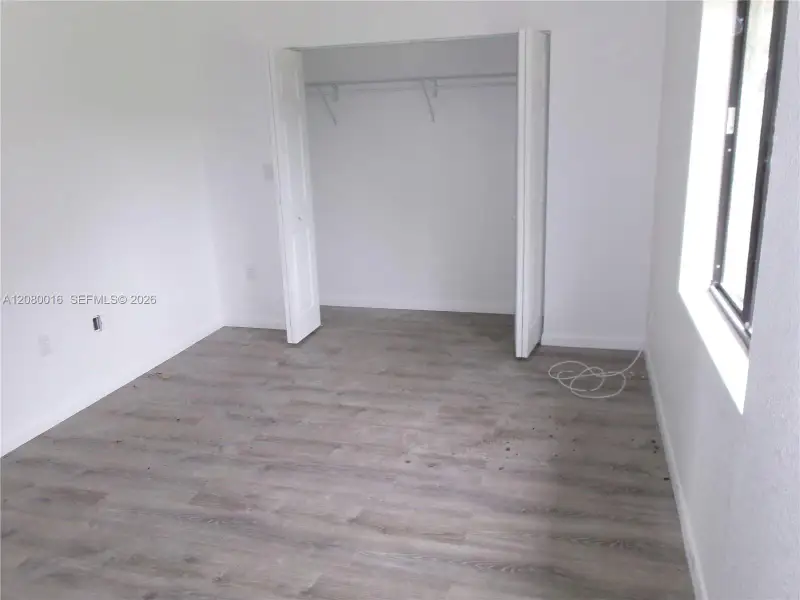 Neutral-toned wood-finish flooring, white walls, and a closet with bifold doors and built-in shelving