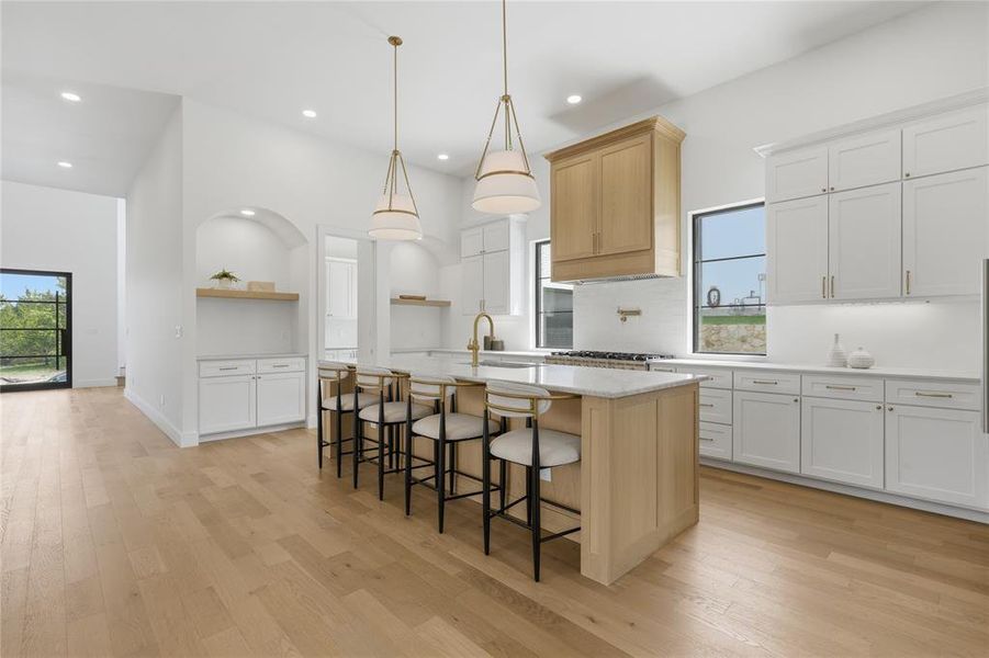 Kitchen featuring an expansive island with seating, pendant lighting, wood-finish flooring, white cabinetry, and stainless steel appliances