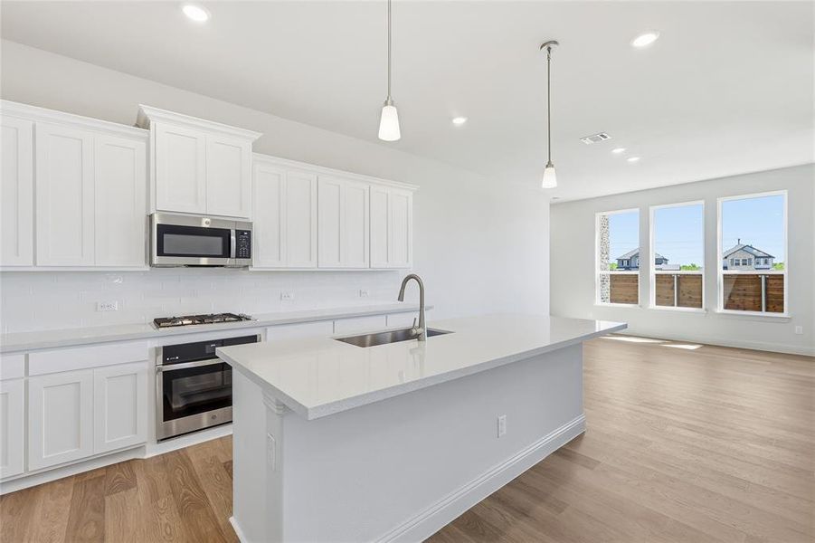 Kitchen with stainless steel appliances, white cabinetry, a kitchen island with sink, and light wood-style floors