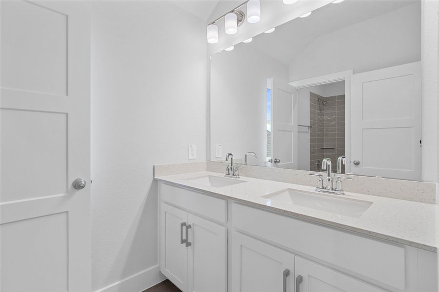 This well-appointed secondary bathroom offers exceptional functionality with its white stained cabinet topped with pristine white countertops and convenient dual undermount sinks. Sleek, polished fixtures complement the expansive vanity mirror and chic light vanity fixture.