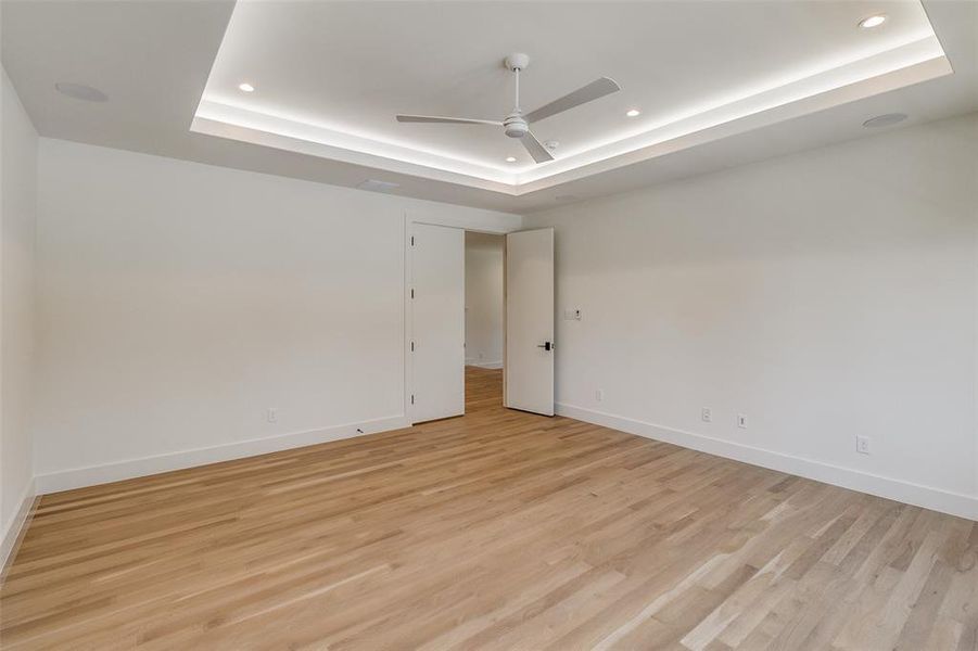 Empty room with a raised ceiling, light wood-style floors, recessed lighting, and ceiling fan Empty room with a raised ceiling, light wood-style floors, recessed lighting, and ceiling fan