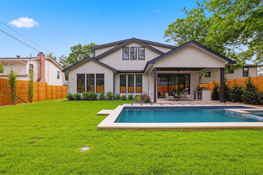 Spacious backyard featuring a rectangular swimming pool with integrated spa, a covered outdoor living area, an outdoor kitchen with built-in grill, a large lawn, and horizontal wood fencing