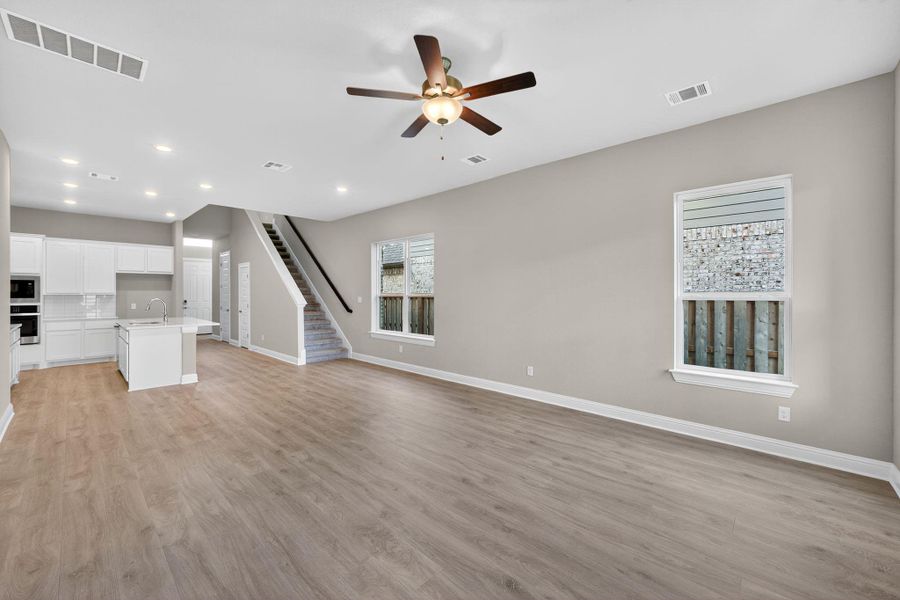 Unfurnished living room with stairs, light wood-type flooring, a ceiling fan, and recessed lighting Unfurnished living room with stairs, light wood-type flooring, a ceiling fan, and recessed lighting