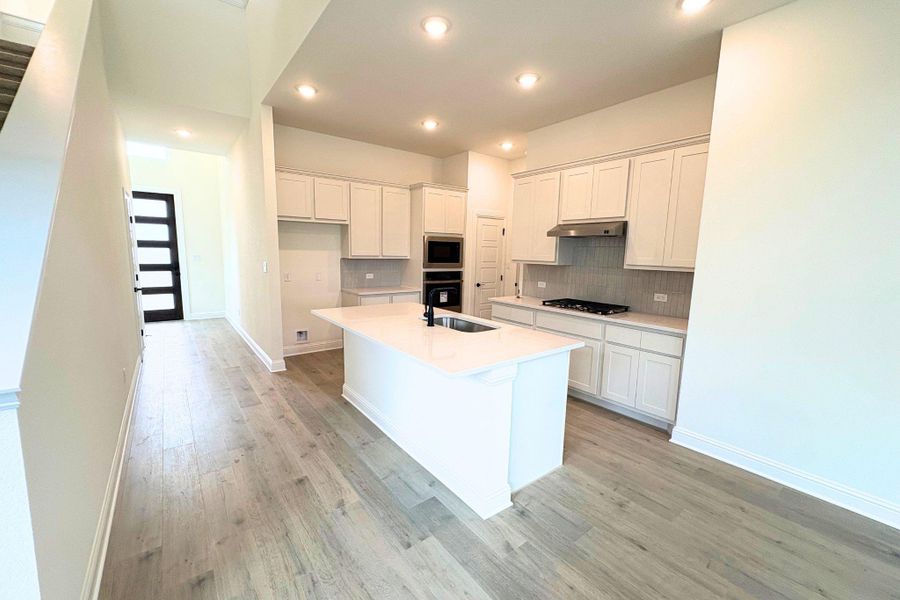 Gleaming wood floors anchor this open kitchen featuring a central island and recessed lighting. Gleaming wood floors anchor this open kitchen featuring a central island and recessed lighting.