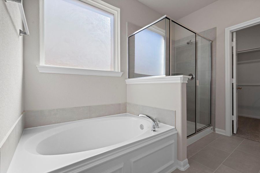 This additional view of your primary bathroom features tile flooring, fresh paint, walk-in shower, a separate garden tub, and a large walk-in closet.