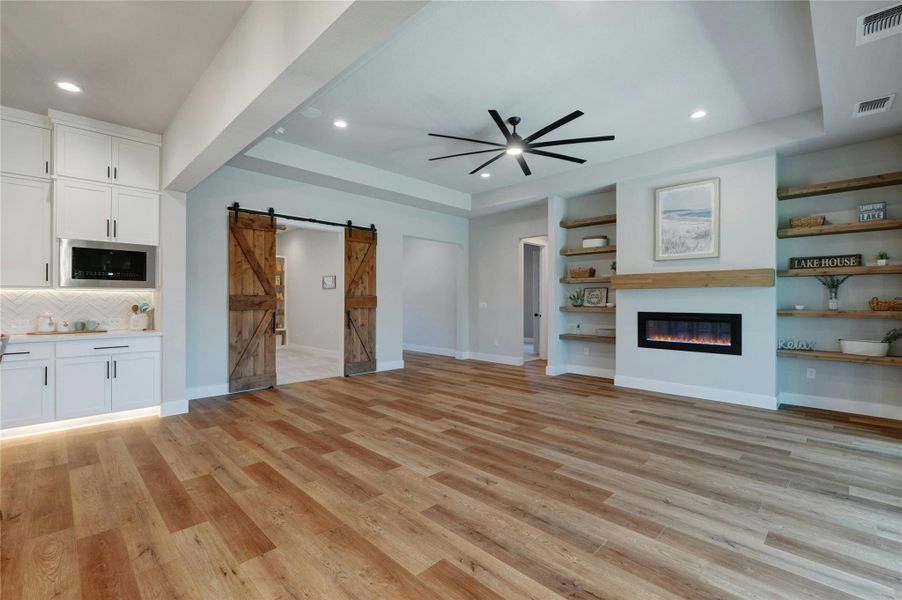 Spacious living area featuring wood-finish flooring, a contemporary electric fireplace with a wood mantle, and built-in shelving