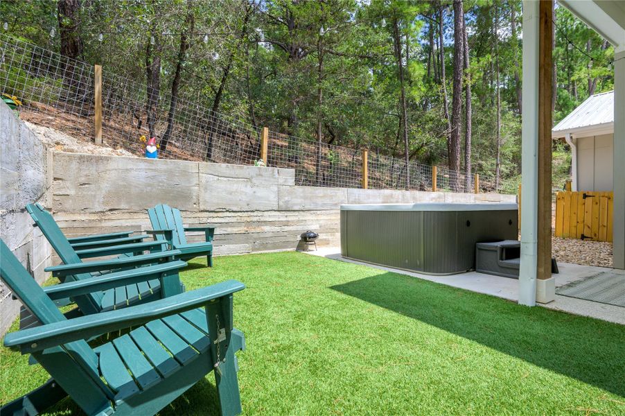 Fenced backyard with a hot tub, a patio area, turf, firepit and surrounded by pine trees!
