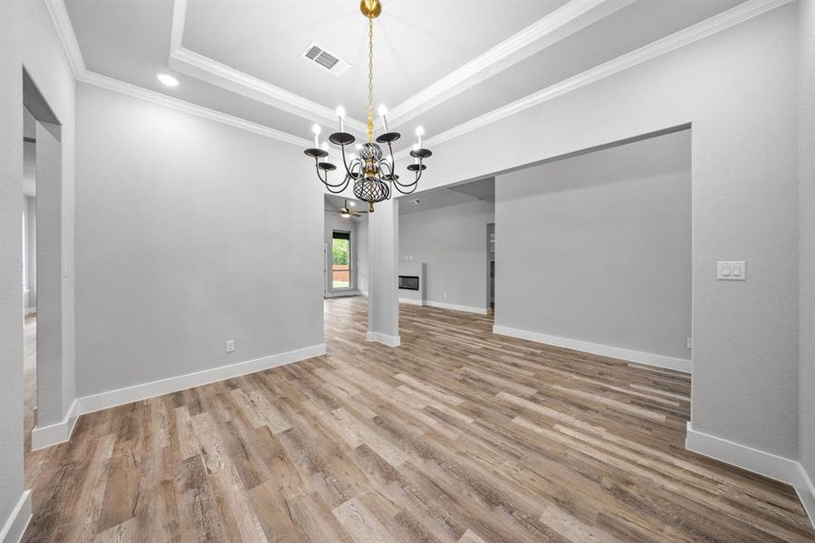 Unfurnished dining area featuring a raised ceiling, ornamental molding, light wood-style flooring, a chandelier, and recessed lighting