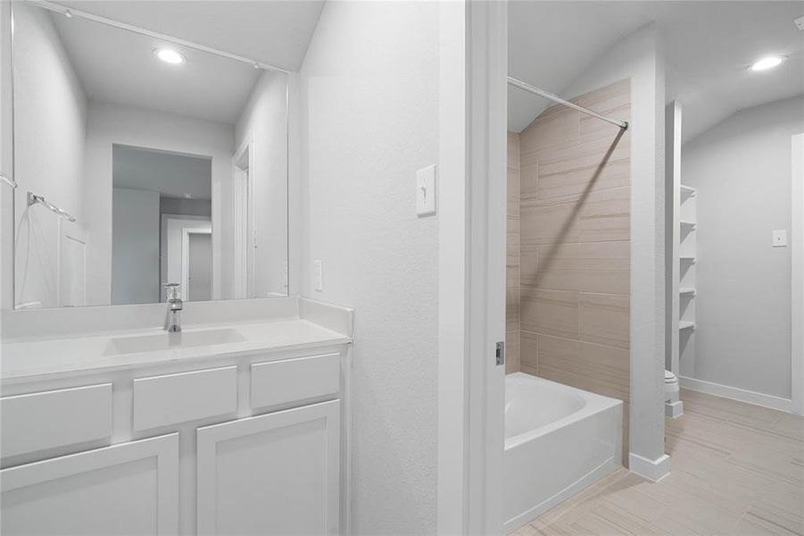 Secondary bath is a jack and jill bathroom featuring tile flooring, bath/shower combo with tile surround, white stained wood cabinets, beautiful light countertops, mirror, sleek fixtures and modern finishes.