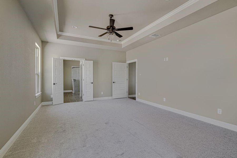 Unfurnished bedroom featuring a raised ceiling, light colored carpet, and ceiling fan