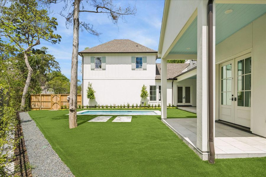 Additional green space with expansive turf surrounding the pool, offering flexible room for outdoor activities and relaxation. This covered patio overlooks the backyard while fencing maintains privacy along the wooded ravine perimeter.