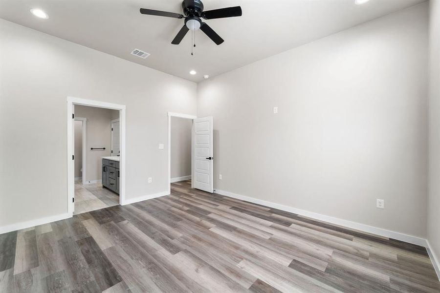 Unfurnished bedroom with ceiling fan, a high ceiling, light wood-type flooring, and ensuite bath