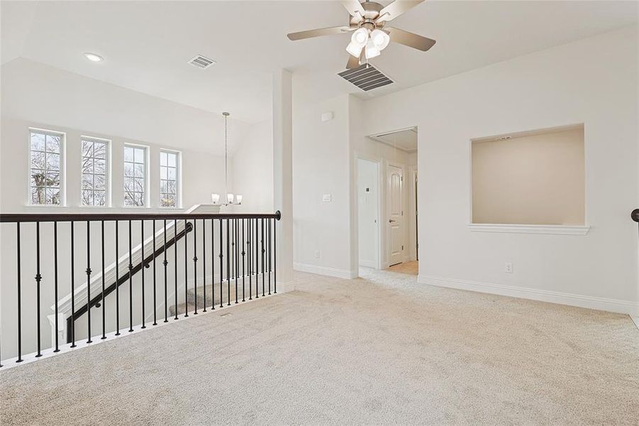 Carpeted empty room featuring ceiling fan with notable chandelier