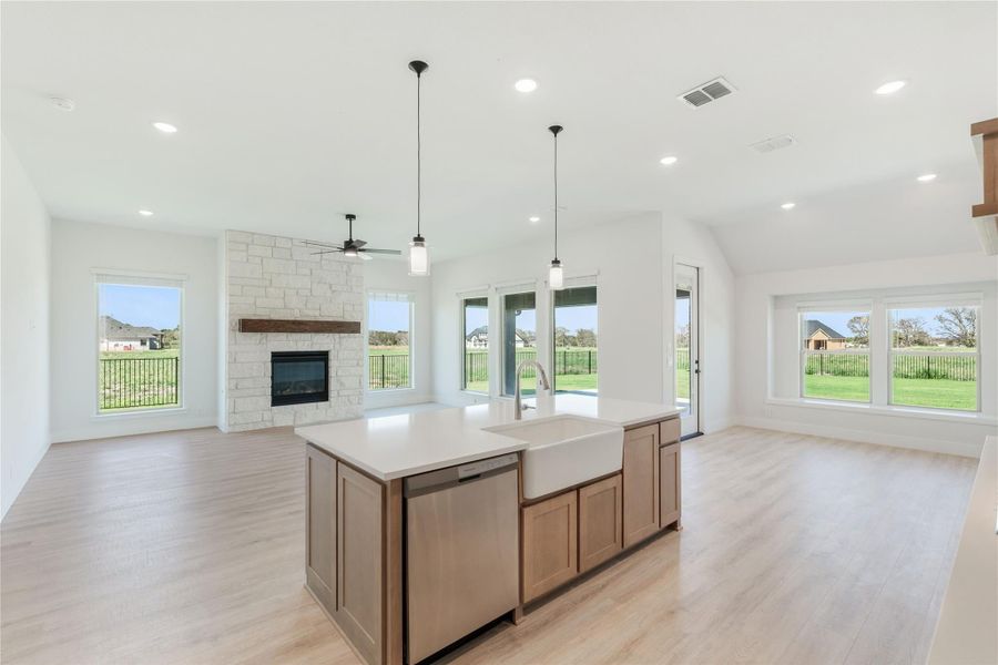 Open-concept kitchen with center island, farmhouse sink, and stone fireplace in living area beyond