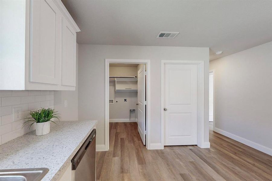 Kitchen featuring light stone countertops, dishwasher, light hardwood / wood-style flooring, and white cabinets