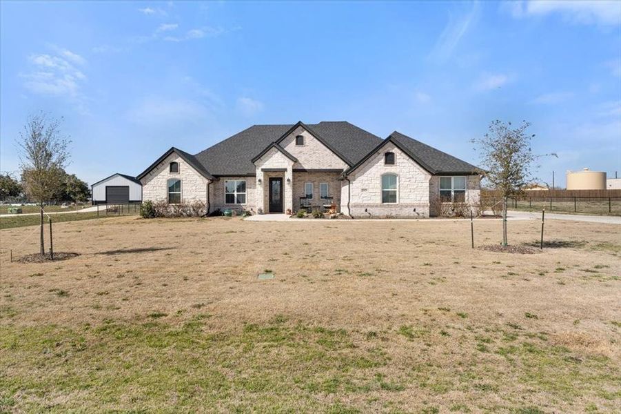 French provincial home featuring a front yard, stone siding, roof with shingles, and fence