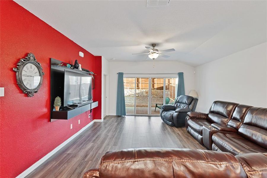 Living room featuring visible vents, ceiling fan, baseboards, vaulted ceiling, and wood finished floors