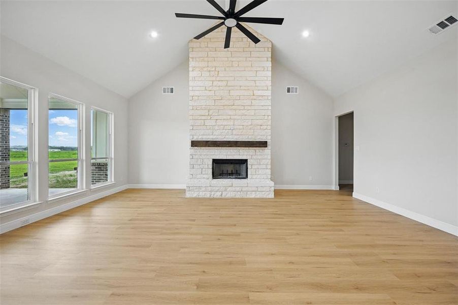 Unfurnished living room featuring ceiling fan, high vaulted ceiling, light wood finished floors, and a stone fireplace Unfurnished living room featuring ceiling fan, high vaulted ceiling, light wood finished floors, and a stone fireplace