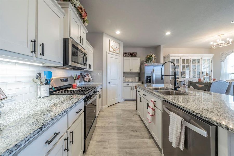 Kitchen featuring white cabinets, sink, decorative backsplash, a notable chandelier, and stainless steel appliances