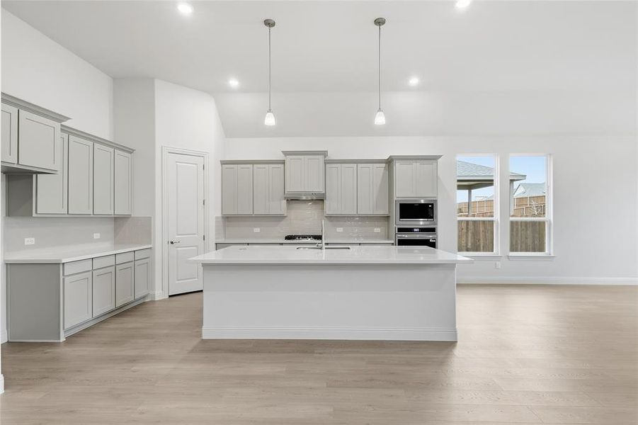 Kitchen featuring gray cabinetry, tasteful backsplash, an island with sink, light wood-type flooring, and stainless steel appliances