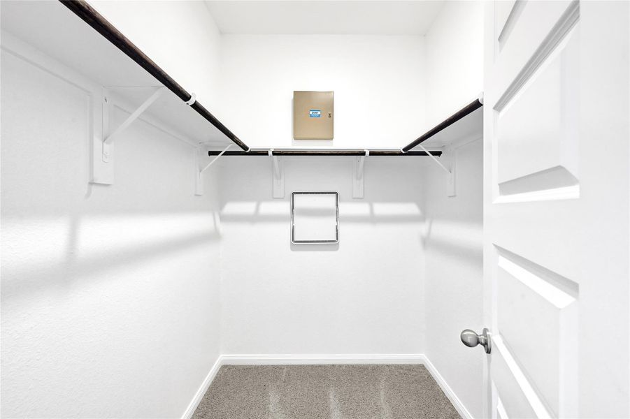 This photo shows a spacious, well-lit walk-in closet with white walls, carpeted flooring, and ample hanging space.Please note: The image is not the actual home; it is a home with the same floor plan in the neighborhood.