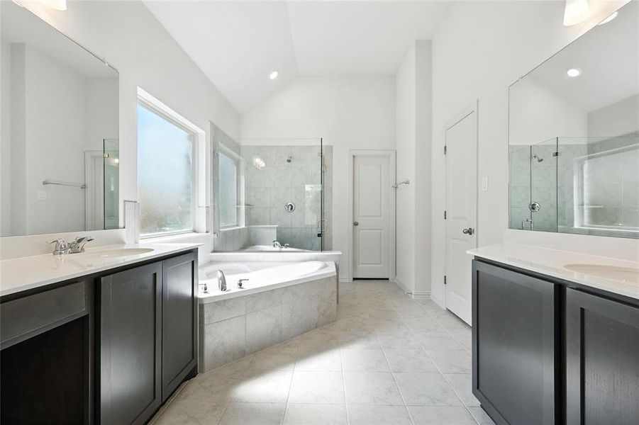 Bathroom featuring a shower stall, a bath, two vanities, light tile patterned floors, and lofted ceiling