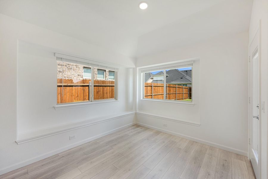 Empty room with white walls, light wood floors, and two windows overlooking a backyard fence Empty room with white walls, light wood floors, and two windows overlooking a backyard fence