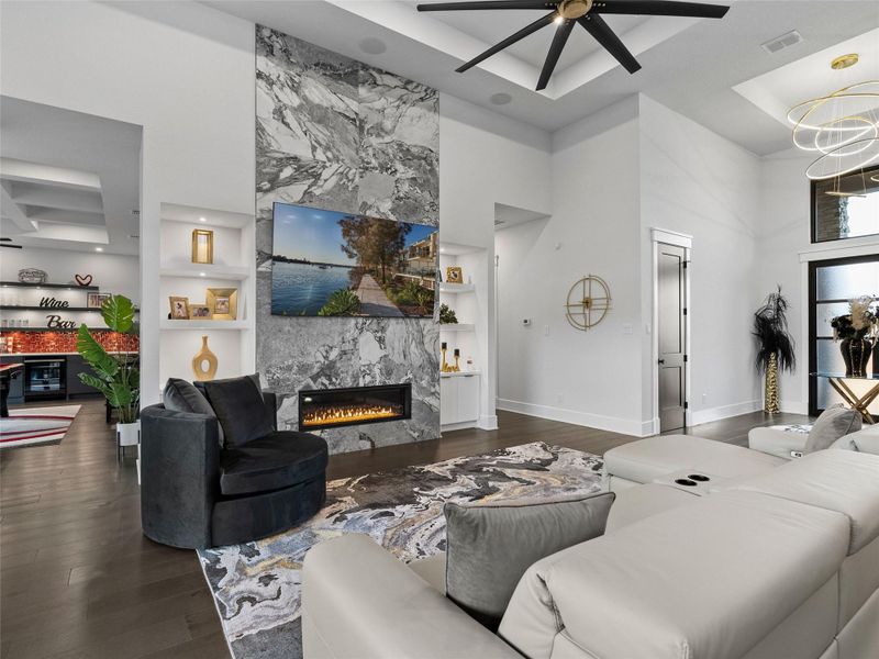 Living area with dark wood-style flooring, a high end fireplace, a high tray ceiling, suspended lighting, and ceiling fan