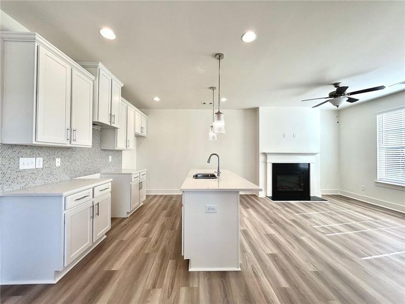 Kitchen with sink, light hardwood / wood-style floors, a kitchen island with sink, ceiling fan, and decorative light fixtures