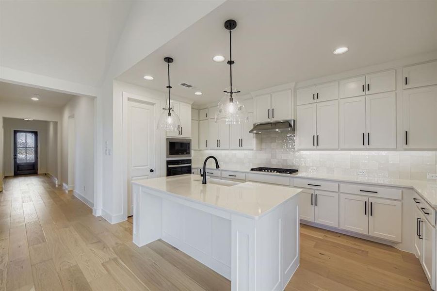 Kitchen with recessed lighting, light wood-style flooring, an island with sink, decorative backsplash, and white cabinets Kitchen with recessed lighting, light wood-style flooring, an island with sink, decorative backsplash, and white cabinets