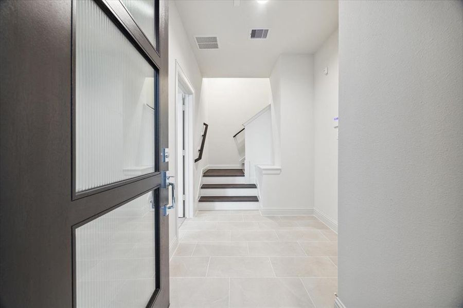 The inviting entryway of this modern home sets the tone for the stylish interiors. Clean tile flooring and an open layout create a bright and welcoming space. Just inside the entrance, you are greeted by a sleek staircase that leads to the main living areas and a first-floor bedroom, offering a harmonious flow between the floors. The design is minimal yet functional, providing a smooth transition from the outdoors into the home.