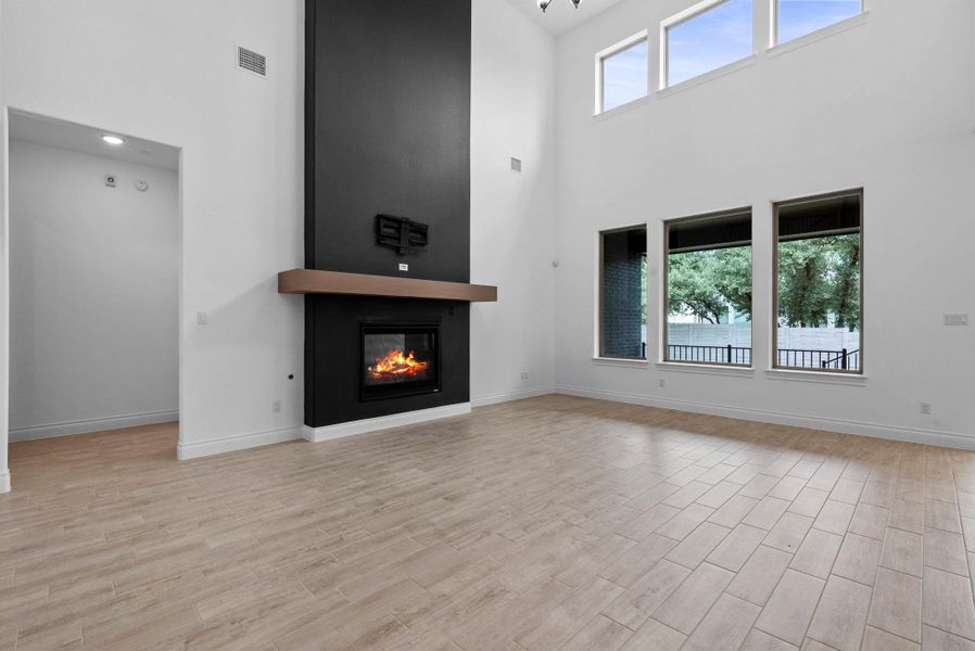 Spacious living room featuring a modern black fireplace, abundant natural light from oversized windows, and high ceilings.