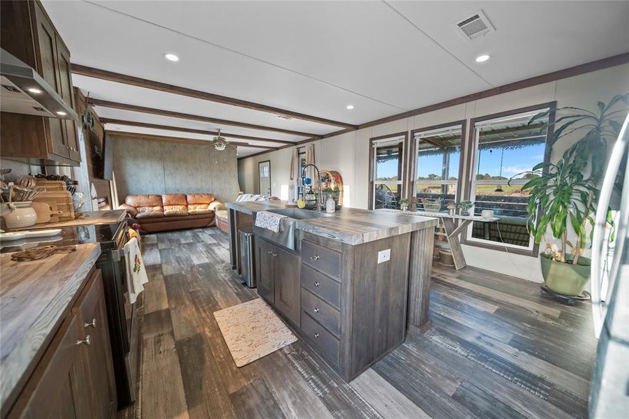 Kitchen featuring dark brown cabinetry, wood counters, beamed ceiling, stainless steel appliances, and dark wood-style flooring Kitchen featuring dark brown cabinetry, wood counters, beamed ceiling, stainless steel appliances, and dark wood-style flooring