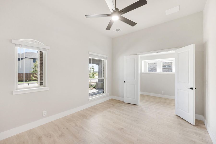 Empty bedroom with light wood floors, ceiling fan, and two windows with natural light
