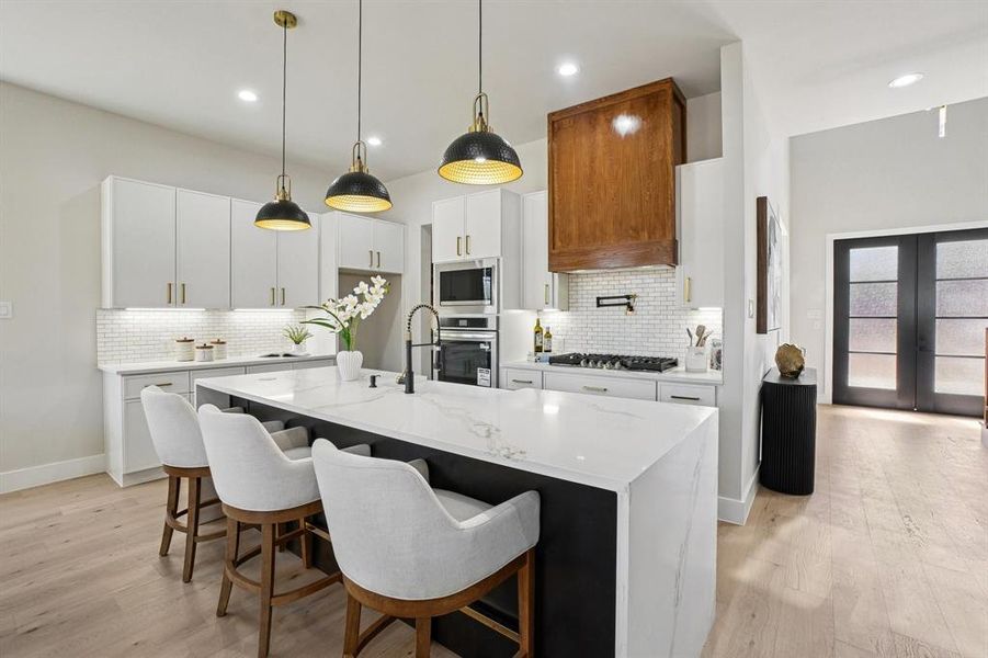 Dual tone kitchen featuring a kitchen breakfast bar, light stone counters, pendant lighting, light wood-type flooring, and two tone cabinetry