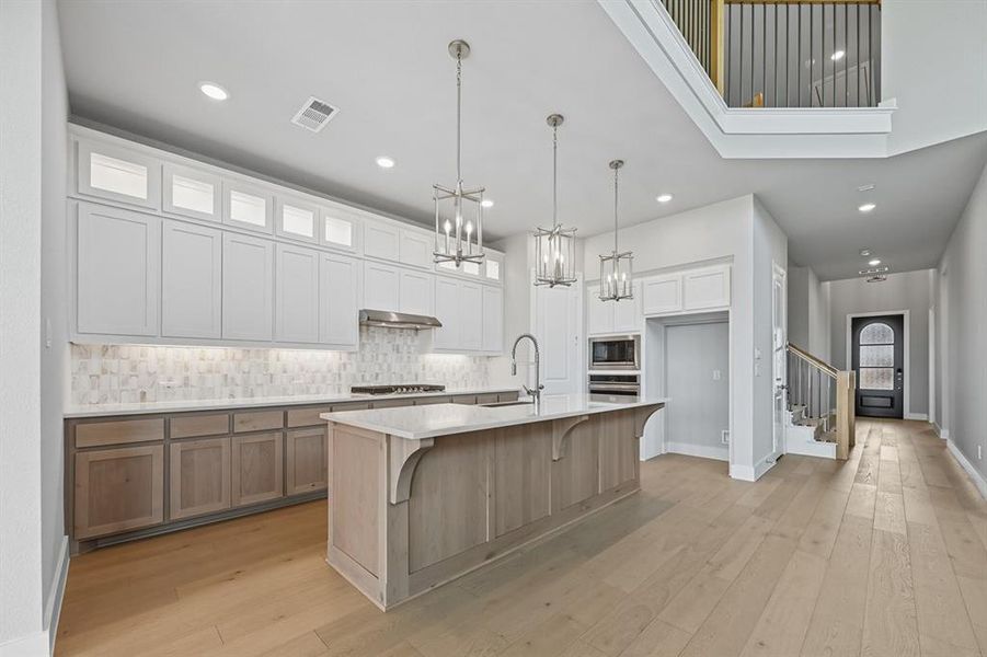 Kitchen with backsplash, glass insert cabinets, light wood-style floors, white cabinets, and pendant lighting