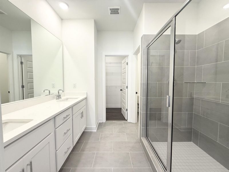 Full bath with double vanity, a walk in closet, a shower stall, light tile patterned floors, and recessed lighting
