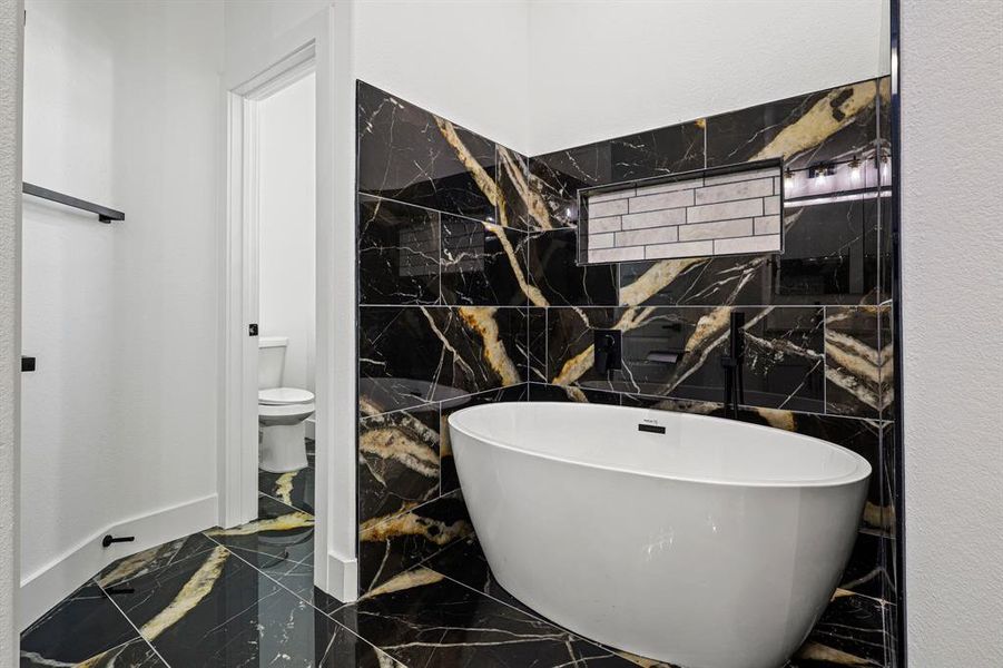 Full bath with toilet, a freestanding tub, and marble finish floor