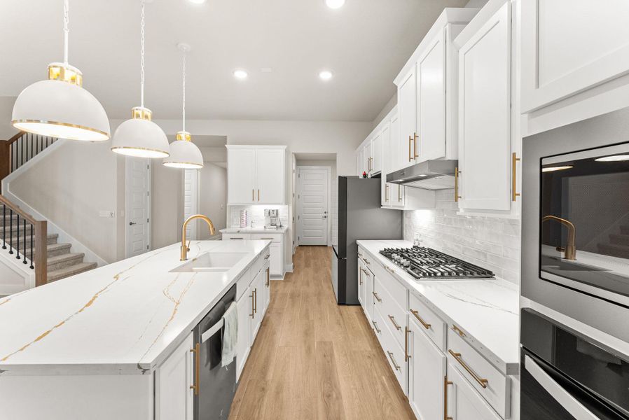 The island kitchen has Silestone counters, 42” Shaker style cabinets with gold hardware, pendant lights, breakfast bar, tile backsplash and walk-in pantry. The stainless steel appliances include a five-burner cooktop, oven, microwave, dishwasher, and vent hood.