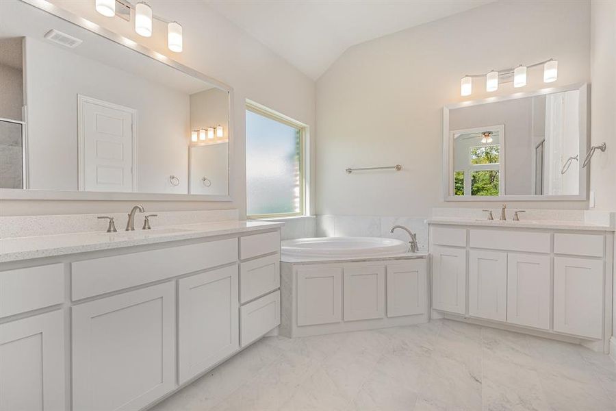Bathroom featuring a garden tub, vaulted ceiling, two vanities, light marble finish flooring, and a stall shower Bathroom featuring a garden tub, vaulted ceiling, two vanities, light marble finish flooring, and a stall shower