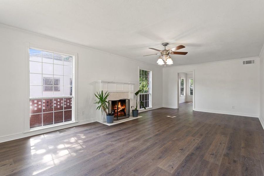 Unfurnished living room featuring dark wood-style flooring, a ceiling fan, a high end fireplace, crown molding, and baseboards
